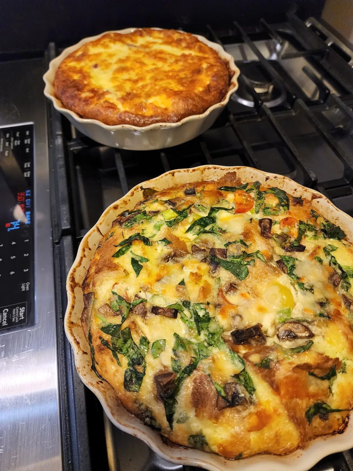 Two freshly baked quiches, one with spinach, mushrooms, and tomatoes